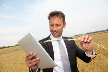 Businessman with electronic tablet in wheat field