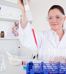 Cute female biologist holding a manual pipette with sample from