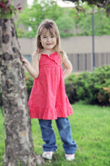 Beautiful little girl in park posing by tree