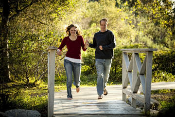Caucasian couple running on outdoor wooden bridge