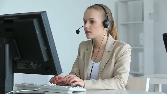Medium shot of young Caucasian female customer support worker typing on computer while answering call, great for support service and marketing visuals