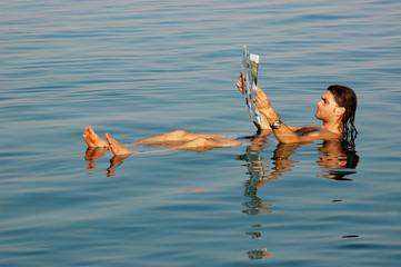 Man floating in a dead sea with newspaper