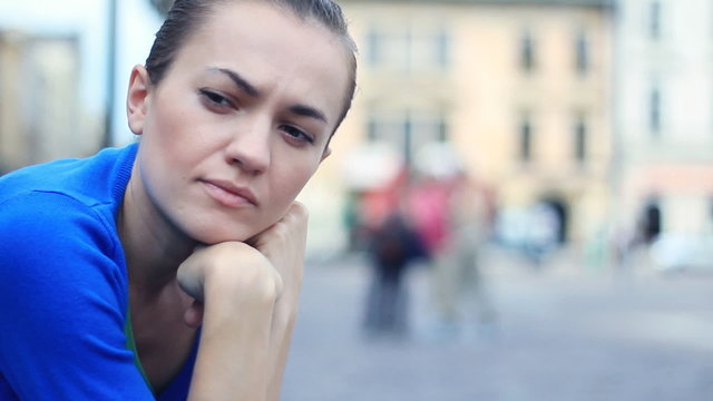 Sad young woman sitting in urban environment, close up