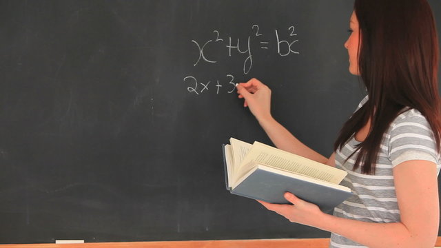 Beautiful woman writing a mathematical formula on a blackboard