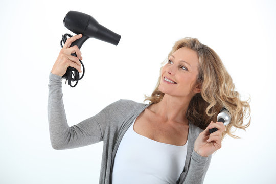 Long haired woman using a hairdryer and large round brush