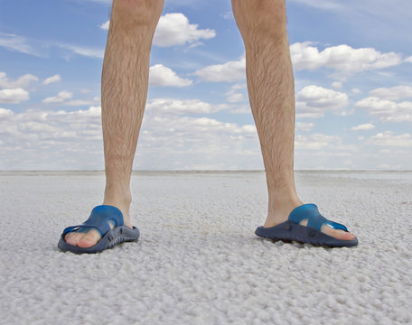 tanned legs of man wearing flip flops standing on the beach