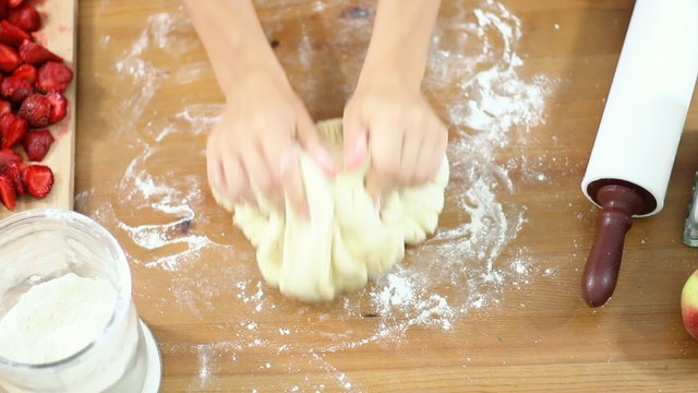 Female hands in flour kneading dough on table, top view