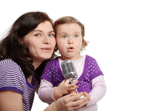 Mother with little daughter cheek to cheek sing into microphone.