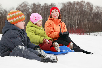 Fototapeta na wymiar young mother, little son and daughter sitting on snow