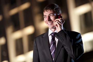 happy businessman talking on cell phone at night city in the bac