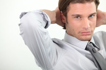 Young businessman sitting with arms behind head.