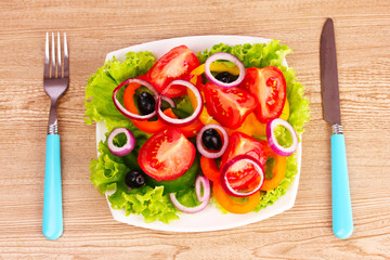 vegetables on a plate and cutlery on a wooden background