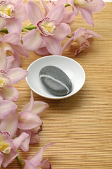 Fototapeta na wymiar Bowl of zen stones with pink orchid over mat