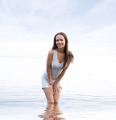 Fototapeta na wymiar A young brunette in a beautiful dress standing in water