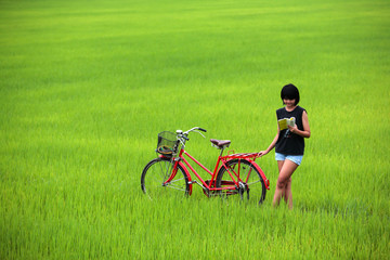 Beautiful girl reading a book with bike in paddy field