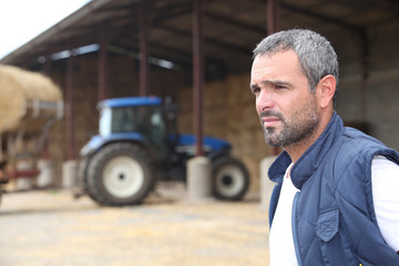 Obraz premium Farmer standing in front of a barn containing a tractor