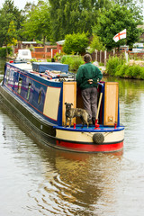 Fototapeta na wymiar Man steering Houseboat along canal with dog on board