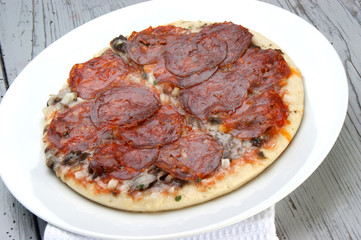 Pizza mit Paprikasalami auf einem weißen Teller