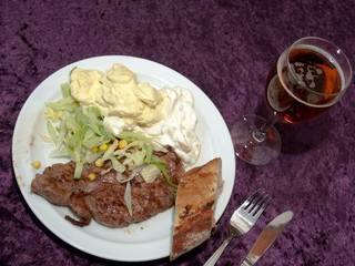 Grilled steak with green salad, potato salad, bread, and a beer