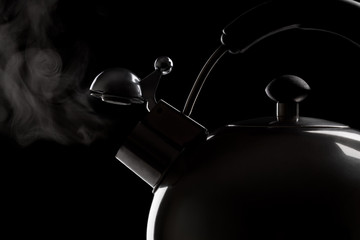 Tea kettle with boiling water over dark background