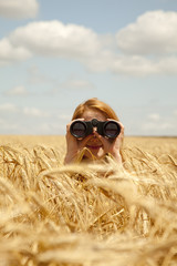 Fototapeta premium Redhead girl with binocular at wheat field.
