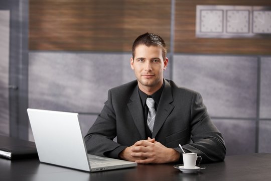 Confident manager sitting in fancy office smiling