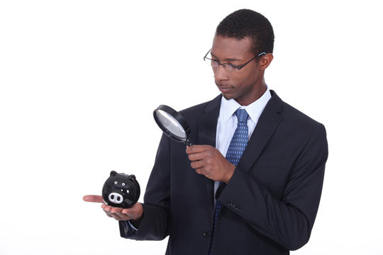 Man examining piggy bank with a magnifying glass