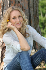 Obraz premium Woman with yellow flower in her hair sitting in front of a tree