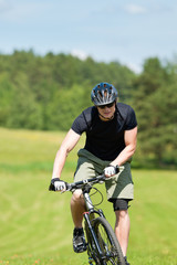 Sportive man mountain biking uphill sunny meadows