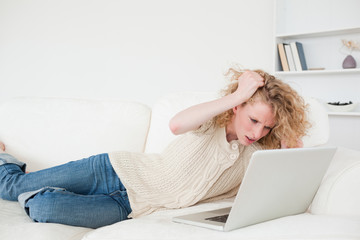 Attractive blonde woman relaxing with her laptop while lying on