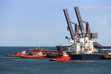 Fototapeta premium Tug boats pushing a cargo ship to port.