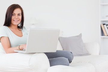 Fototapeta na wymiar Close up of a charming brunette sitting on a sofa using a laptop