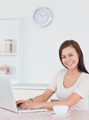 Smiling brunette using her laptop and having a tea