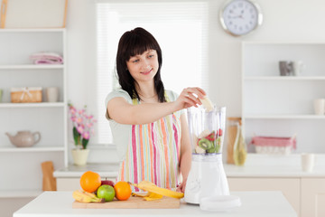 Obraz na płótnie Canvas Gorgeous brunette woman putting vegetables in a mixer while stan