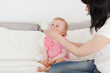 Fototapeta na wymiar Beautiful brunette female bottle-feeding her baby on a bed