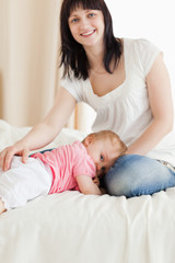 Cute brunette woman posing while her baby is lying on a bed