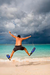 Obraz premium Tanned man jump in blue flippers on sand beach and ocean