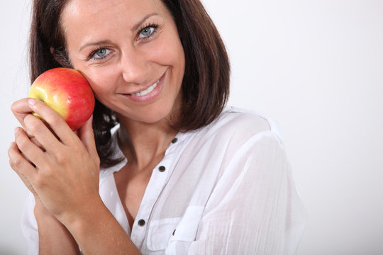 Smiling woman holding an apple to her face