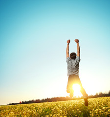 Fototapeta premium Young man jumping on meadow with dandelions on cloudy background