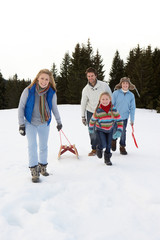Fototapeta na wymiar Young Family Walking Through Snow With Sled