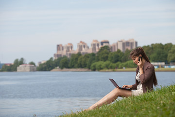 Young woman with laptop and mobile phone in the park.