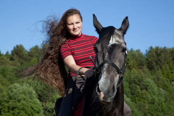 Beautiful girl with brown hair on a black horse