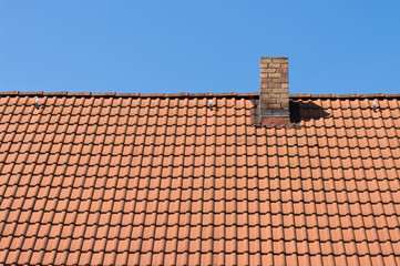 Naklejka premium The roof of tiles and chimney against a blue sky.