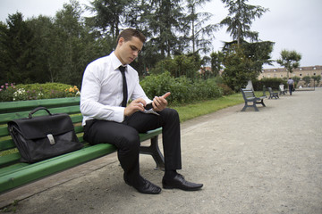 Homme consultant son portable assis sur un banc public.