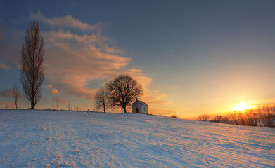Naklejka premium Sunset on frozen field with a chapel and clouds