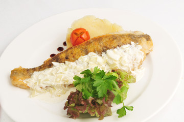 The fried fillet of a cod with a garnish and sauce