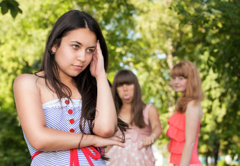 Upset teenage girl with friends gossiping in park