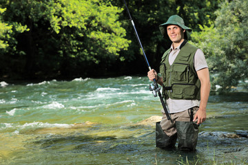 Jeune pêcheur posant avec canne à pêche à la main sur une rivière