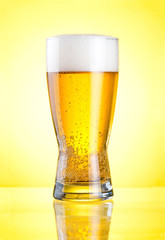 Glass of fresh lager beer close-up with froth over yellow backgr