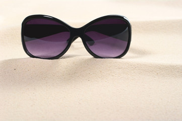 Purple colored sunglasses on sand dunes